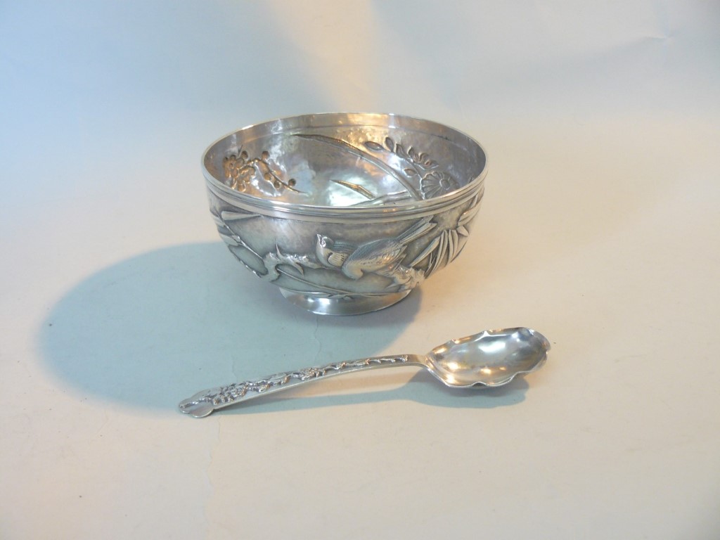 An Oriental white metal bowl, decorated prunus, bamboo and birds; together with a similar spoon,