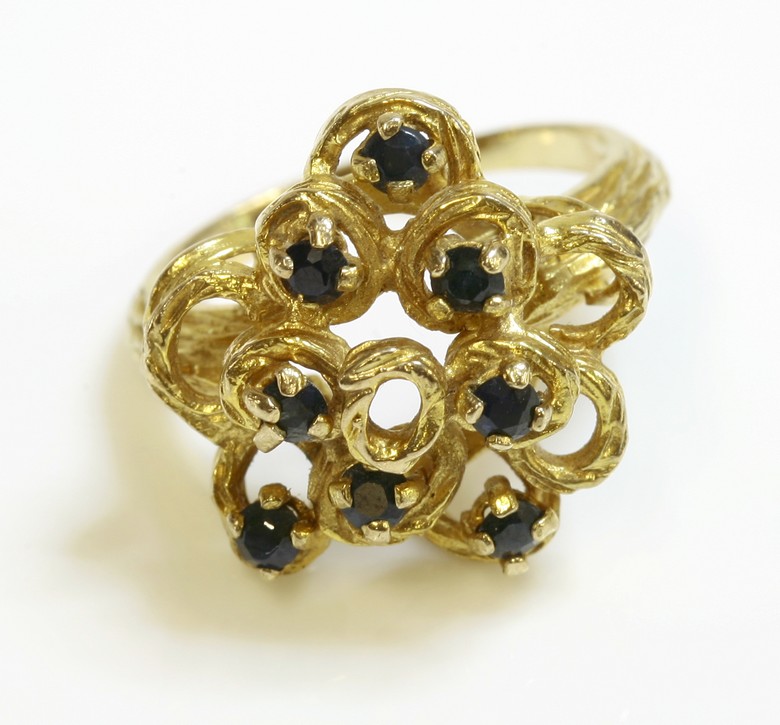 A 9ct gold sapphire ring, c.1970,
with a staggered head, composed of irregular, graduated circles,