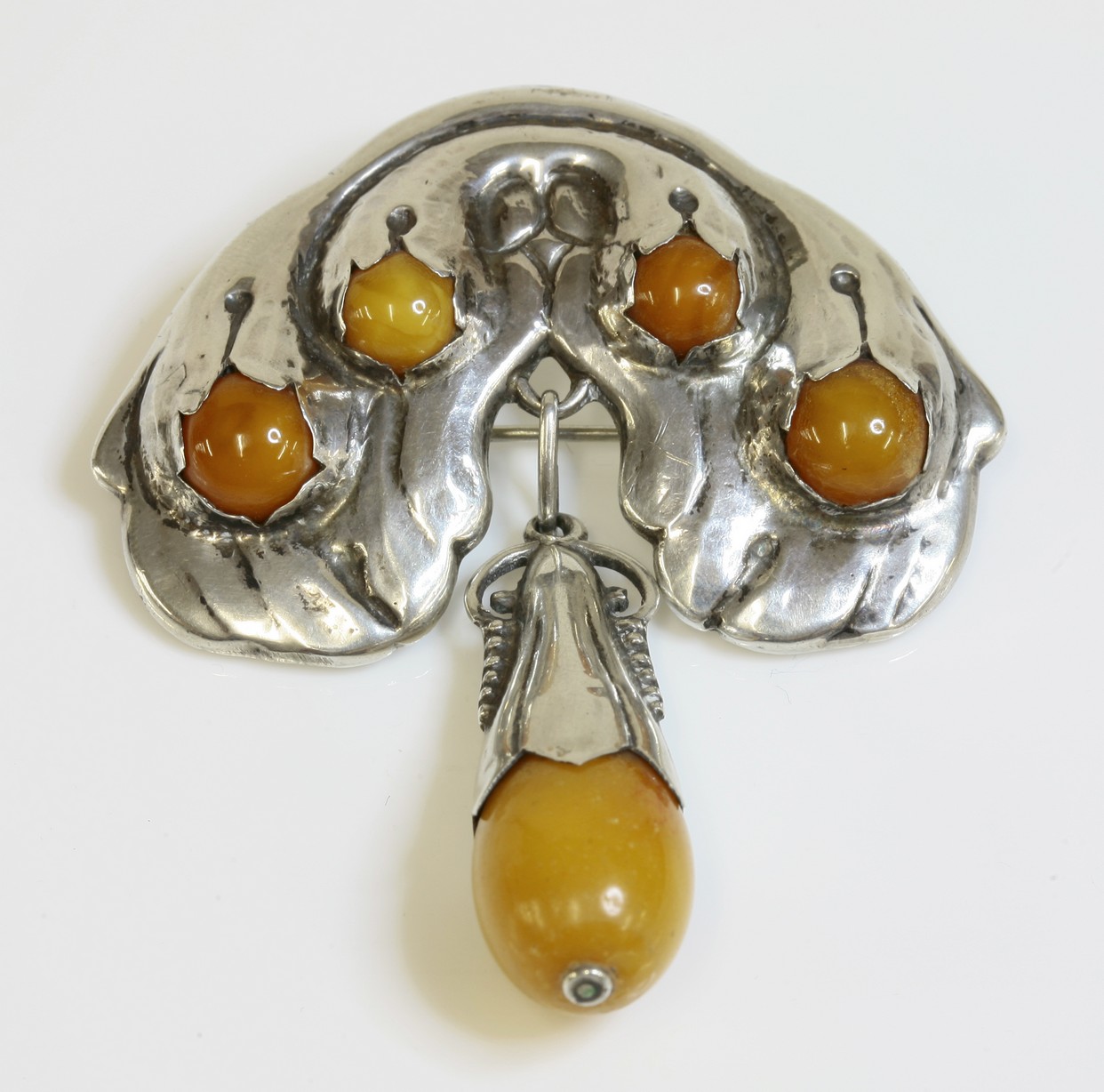 A silver Danish Skonvirke amber brooch,
by Holger Fischer, c.1915, an arched draping foliate top