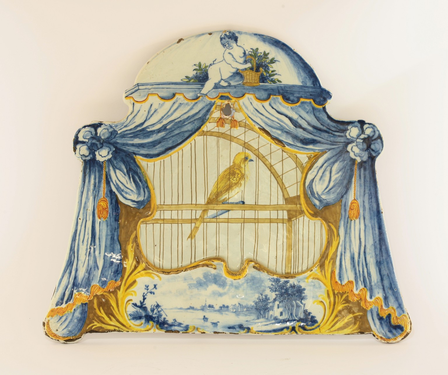 A rare Dutch delft Plaque,  
c.1800, moulded and painted with a caged canary within swept and