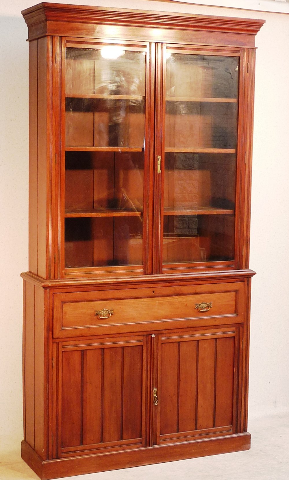 An Edwardian walnut Bookcase, the flaring cornice above two glazed doors enclosing shelves,