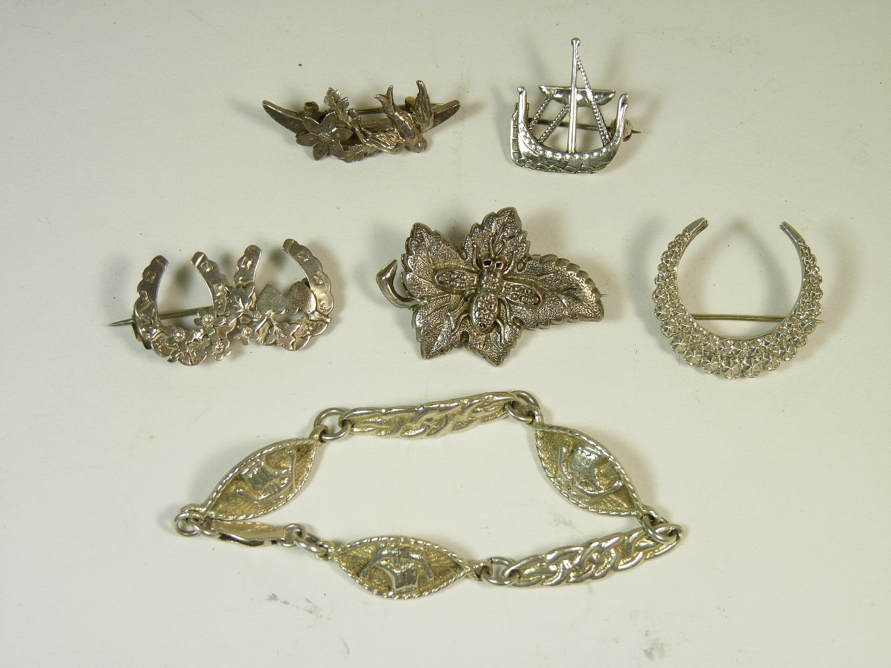 Five decorative silver brooches and a silver bracelet