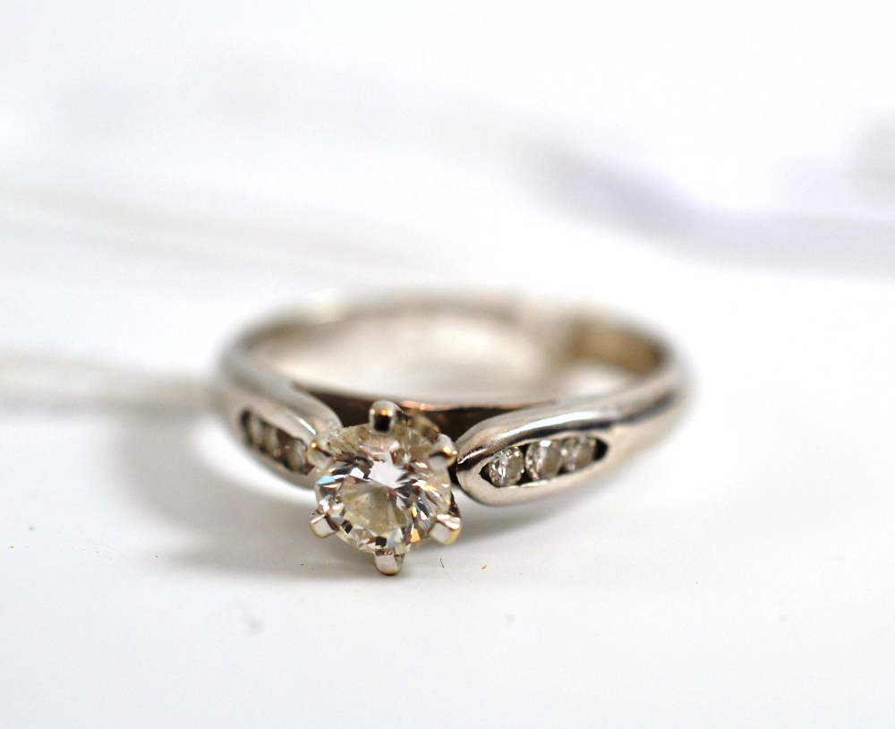 A diamond ring with diamond set shoulders, the round brilliant cut diamond in a white six claw