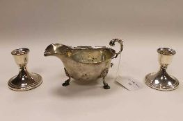 A silver sauce boat, together with a pair of small silver candlesticks. (3)   CONDITION REPORT: