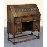 A George V oak bureau, the carved fall flap above a drawer and two cupboards, on barley twist