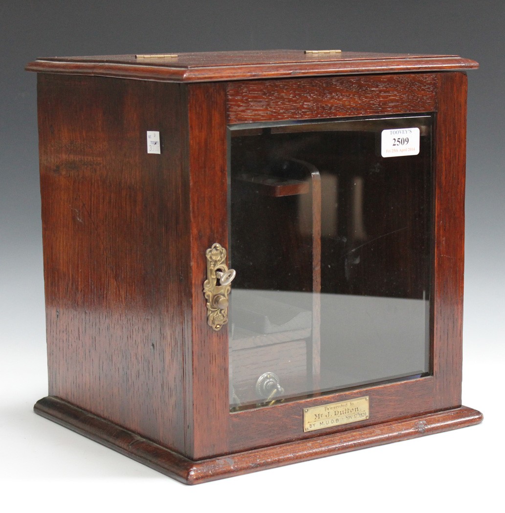 An early 20th Century oak smoker`s cabinet, the single glazed door enclosing a pipe rack and drawer,