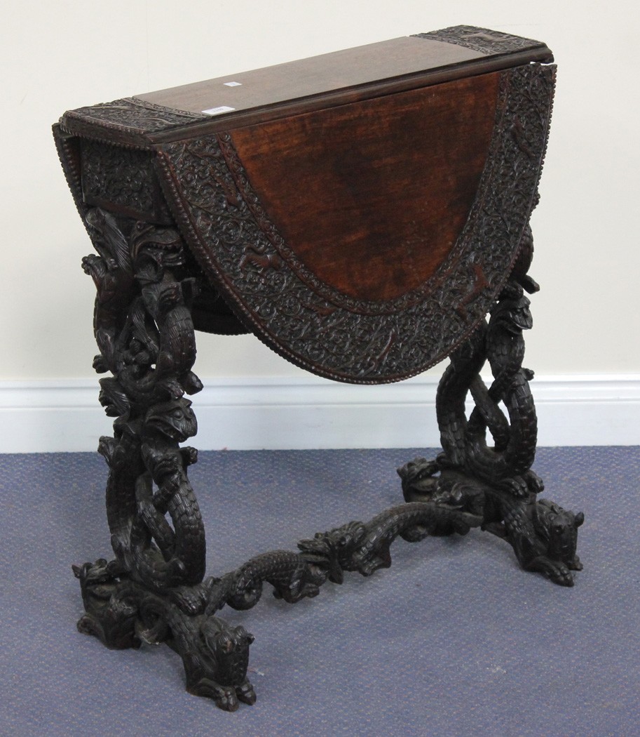 A Goanese carved hardwood oval drop-flap Sutherland table, the top finely carved in relief with a