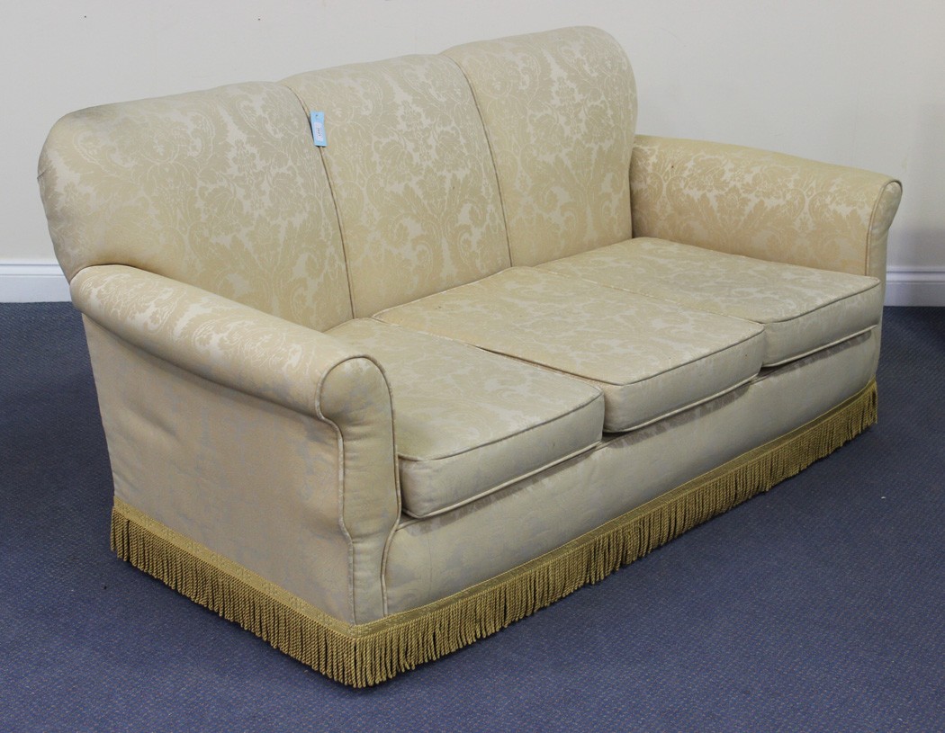 An Edwardian three seat settee upholstered in a patterned cream damask, raised on square tapering