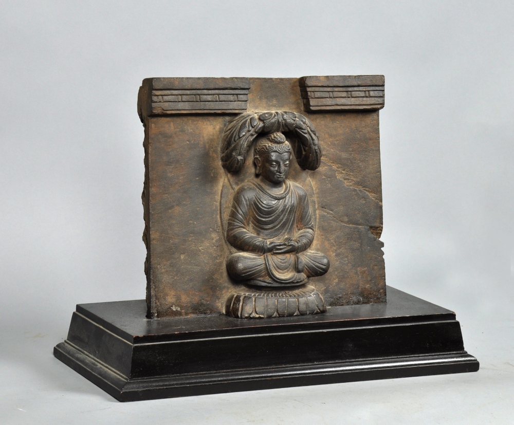 An Indian carved black stone sculpture of a Hindu figure in a meditating position, on wooden