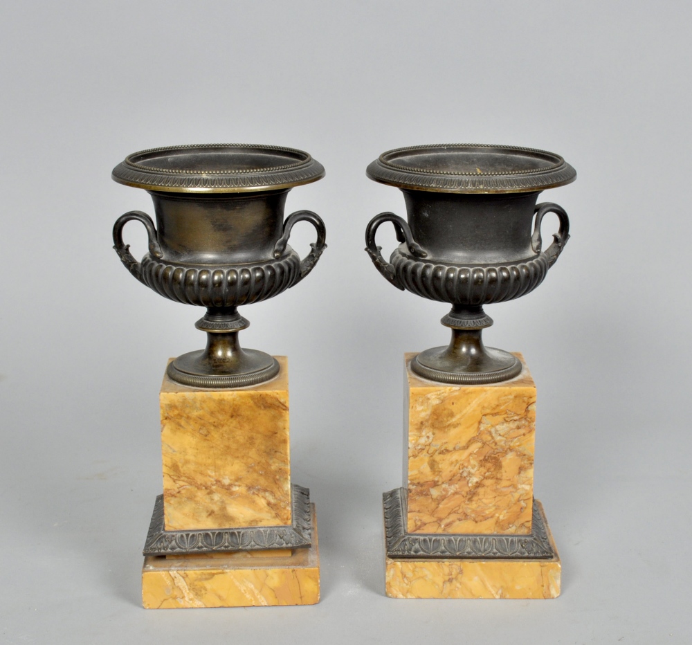 A pair of early 19c bronze two handled urns, lobed and beaded and supported on Sienna marble