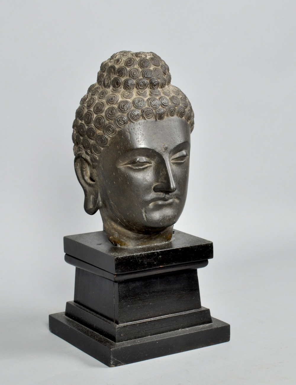 An Indian black stone sculpture of a head, on wooden plinth, the head 10""h, 16"" high overall.