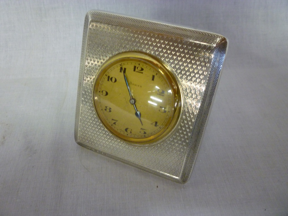 A George V eight-day travelling clock with circular dial in rectangular silver engine turned case,