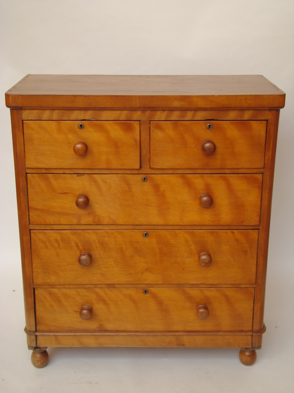 A Victorian satinwood chest of drawers with two short and three long drawers on bun feet.