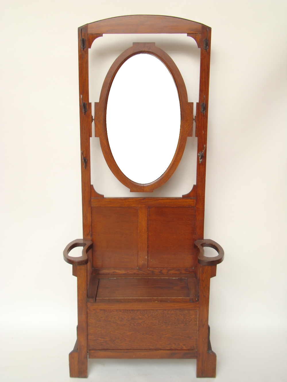 An Edwardian Arts and Crafts oak hall stand, the back with swing mirror, over settle with hinged