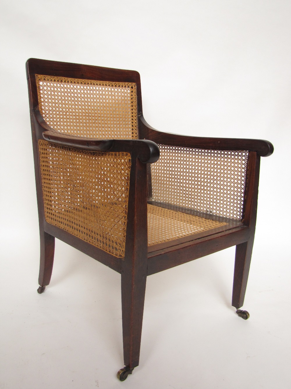 A Regency rosewood bergere library armchair, with square back, arms with rounded terminals and elbow