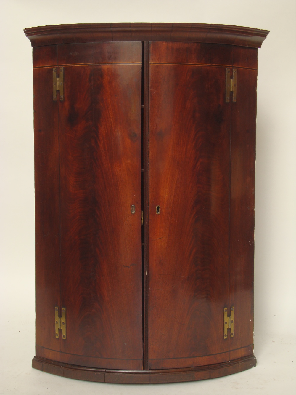 A George III mahogany bowfront hanging corner cupboard, the projecting moulded blockwork cornice