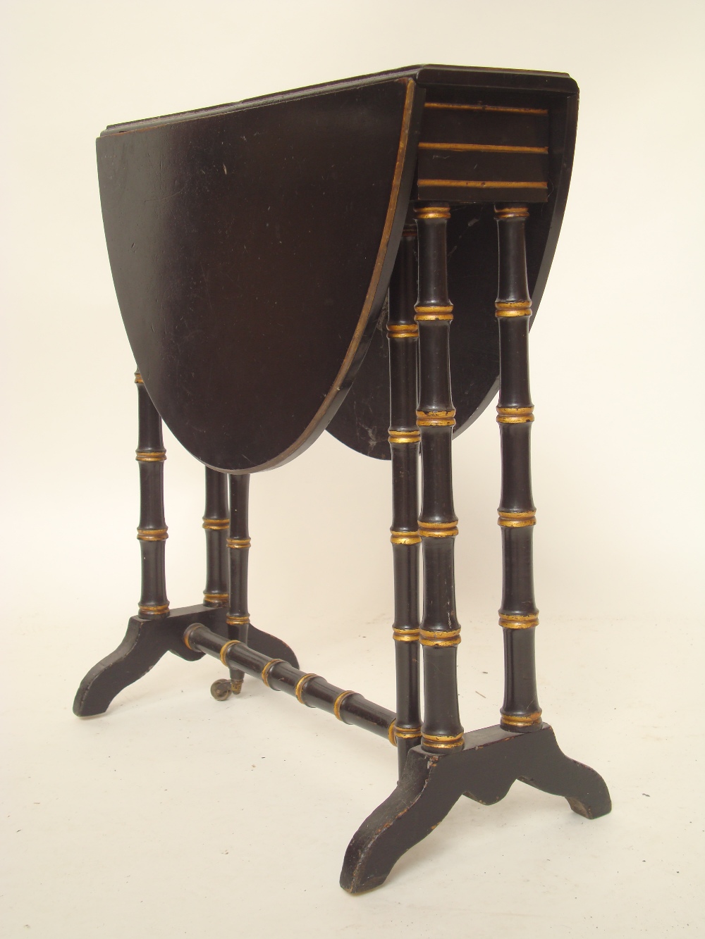 A mid Victorian ebonised and gilt sutherland table, the oval top with moulded edge and twin hinged