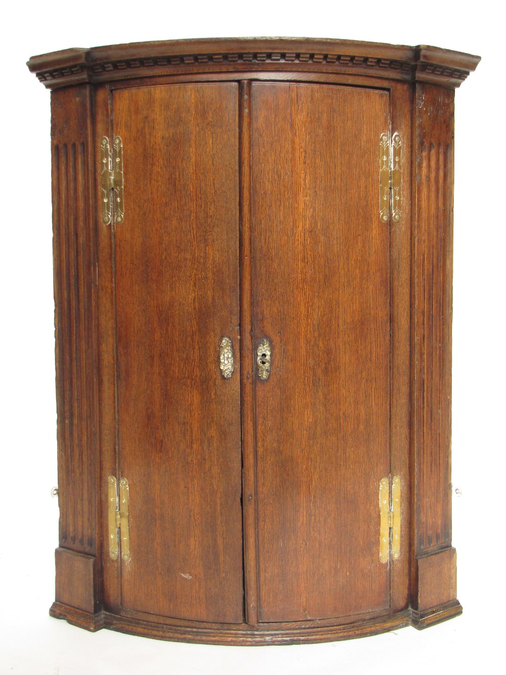 WITHDRAWN.  A George III oak bowfront hanging corner cupboard, the projecting dentil cornice over