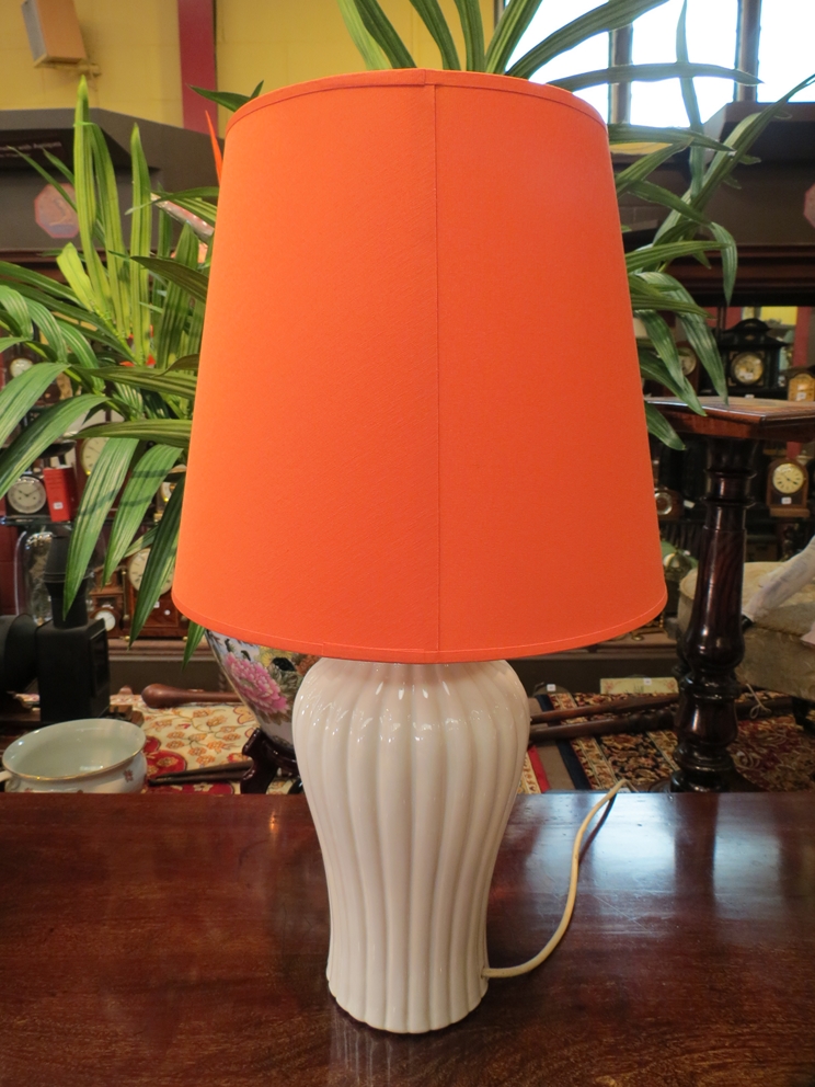 A modern white ceramic lamp base with fluted body and orange shade