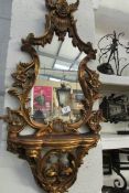 An ornate gilt framed mirror with rose decoration and shelf