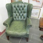A green leathed buttoned wing back armchair