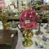 A brass oil lamp with funnel and cranberry glass shade