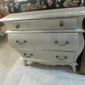 A silver coloured crocodile skin effect 3 drawer bombe chest
