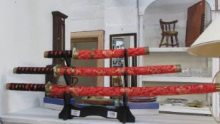 3 Samurai swords with red brocade scabbards on stand