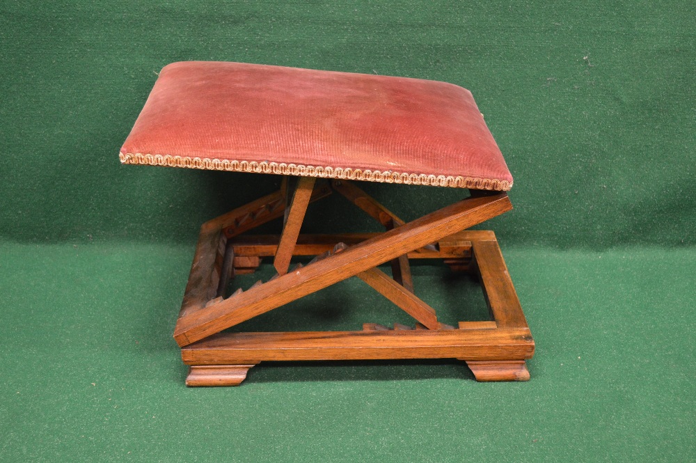 An oak framed adjustable gout stool with padded top and standing on bracket style feet