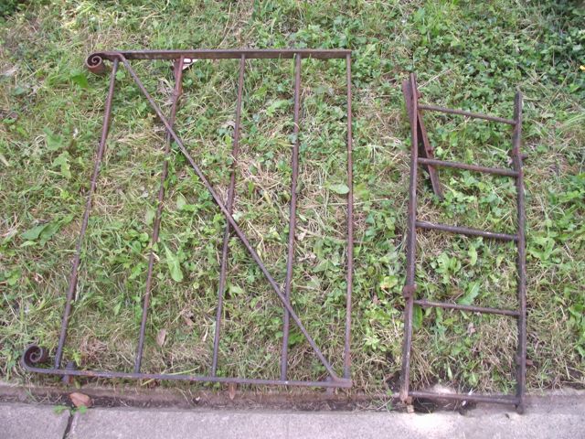 A cast iron pedestrian/garden gate with horizontal rails and scrolled finials