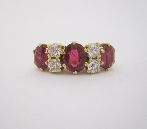 A SYNTHETIC RUBY AND DIAMOND RING claw set to the centre with a row of three oval mixed-cut