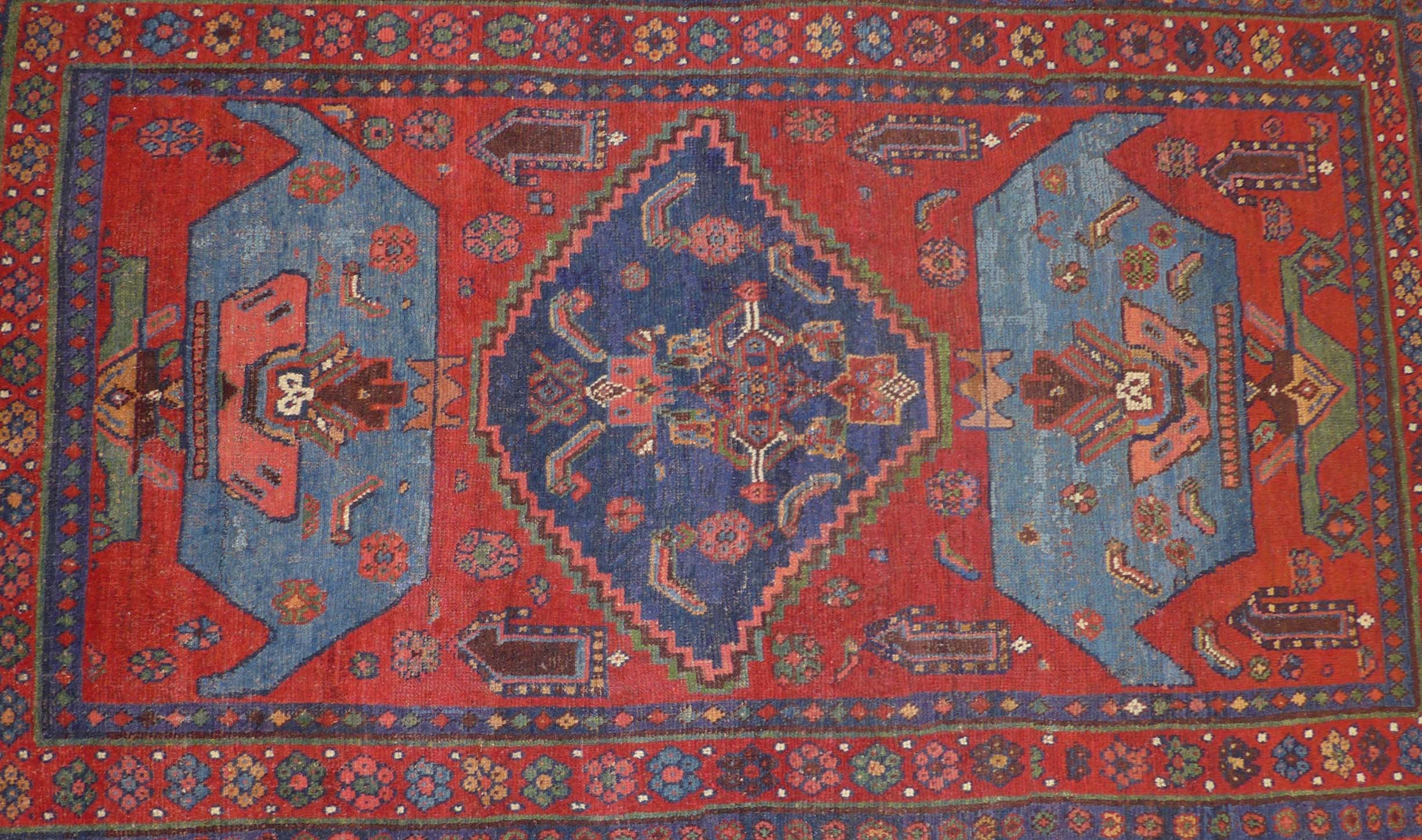 An early 20th century Persian Kurdish rug, on a mainly red ground, the central panel with