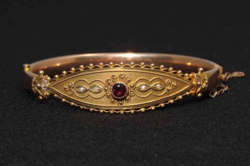 A DECORATIVE HINGED BANGLE, Central collet set circular cut almadine garnet mounted within a