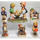 Six Hummel figures of children in various poses and a large figurine of a boy and a girl swinging a