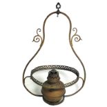 A hanging brass oil lamp with opaque glass shade and scrolling decoration to the sides.
