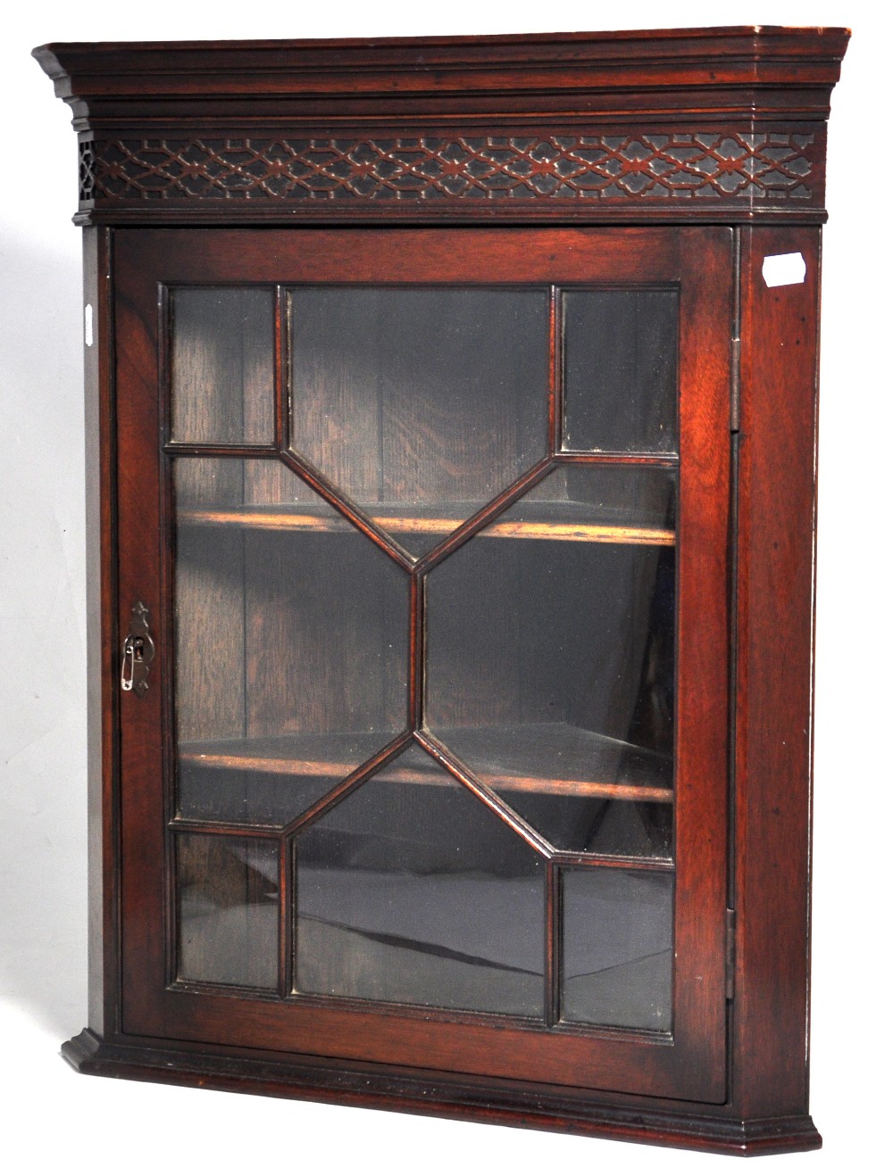 A reproduction mahogany flat fronted hanging corner cupboard with fretwork decorated frieze and