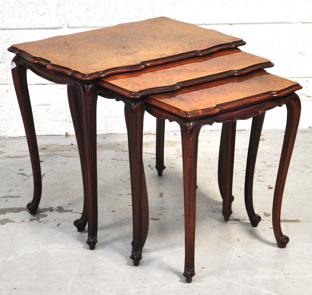 A nest of three shaped walnut occasional tables raised on cabriole legs.