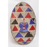 A Namibian oval ceremonial wooden shield centred with a mask and with painted decoration, Namibia,