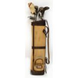 A vintage canvas golf bag containing five simulated hickory shafted golf clubs and various