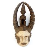 An Igbo helmet mask, Nigeria, with seated figure between tapering horns,