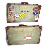Two vintage canvas and leather bound suitcases bearing various shipping labels.