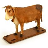 An unusual 19th century papier-mâché toy cow, on wooden base with four wheels, its head tilts to