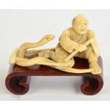 A Japanese Meiji period ivory okimono depicting a kneeling man combating a snake, width 9cm,