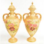 A pair of Royal Worcester twin handled vases with finialled lids, with gilt heightened floral