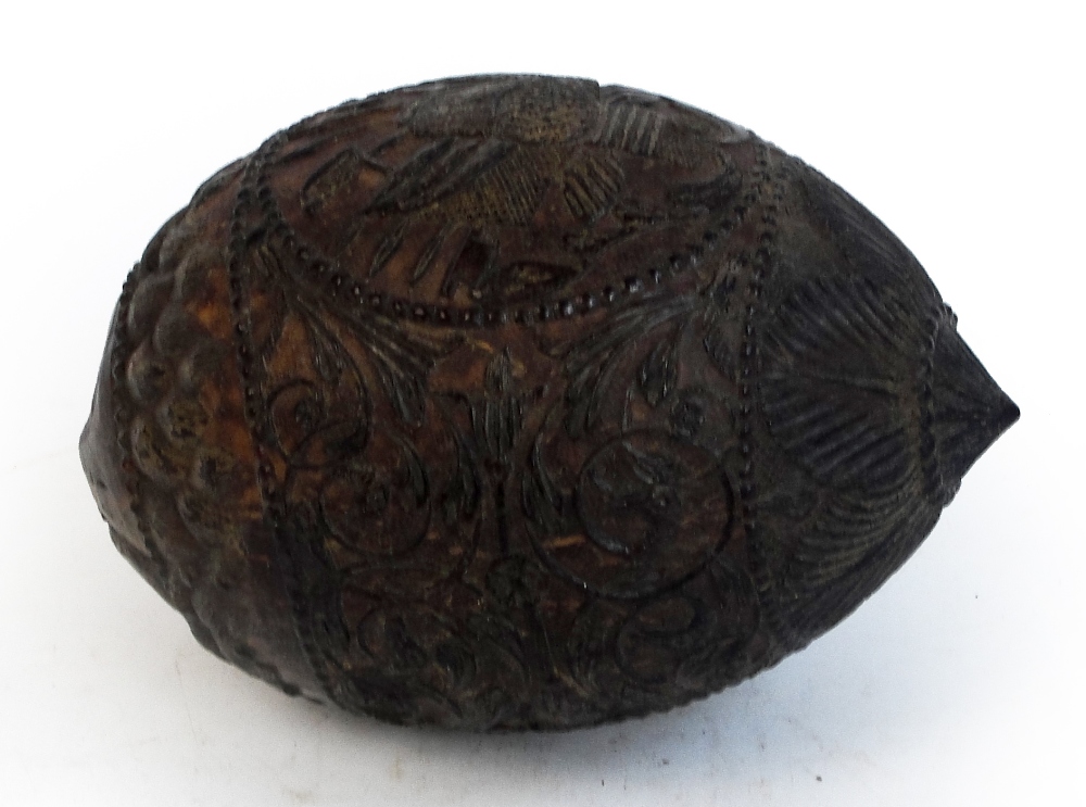 An unusual carved coconut with mask detail to the front and band of scrolling decoration with