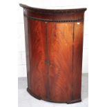 A 18th century mahogany bow front hanging corner cupboard the interior revealing three shelves,