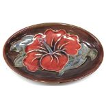 A Moorcroft Hibiscus on red/brown ground oval dish, impressed marks to base, length 11cm.
