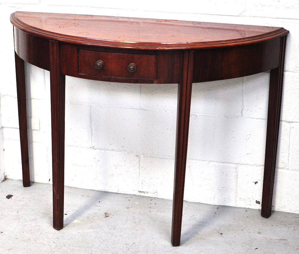 An early 20th century mahogany demi-lune table raised on fluted legs with central single drawer,