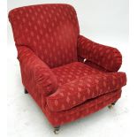 An upholstered armchair raised on turned tapering front legs to brass caps and castors.