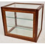 A glazed wooden framed table top display cabinet, the single door enclosing two glass shelves,